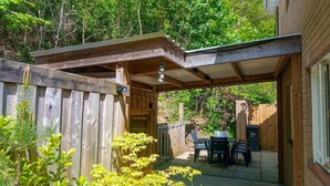A covered patio area with a wooden fence, a table with chairs, and a grill.