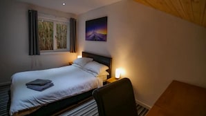 A bedroom with a bed, bedside lamps, a window with curtains, a painting on the wall, and a wooden ceiling.