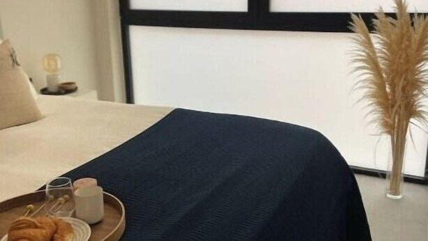 A neatly made bed with a dark blue bedspread, a tray with croissants and a glass of water, and a tall vase with pampas grass. - NordiK 2 - Beautiful apartment close to science (València)