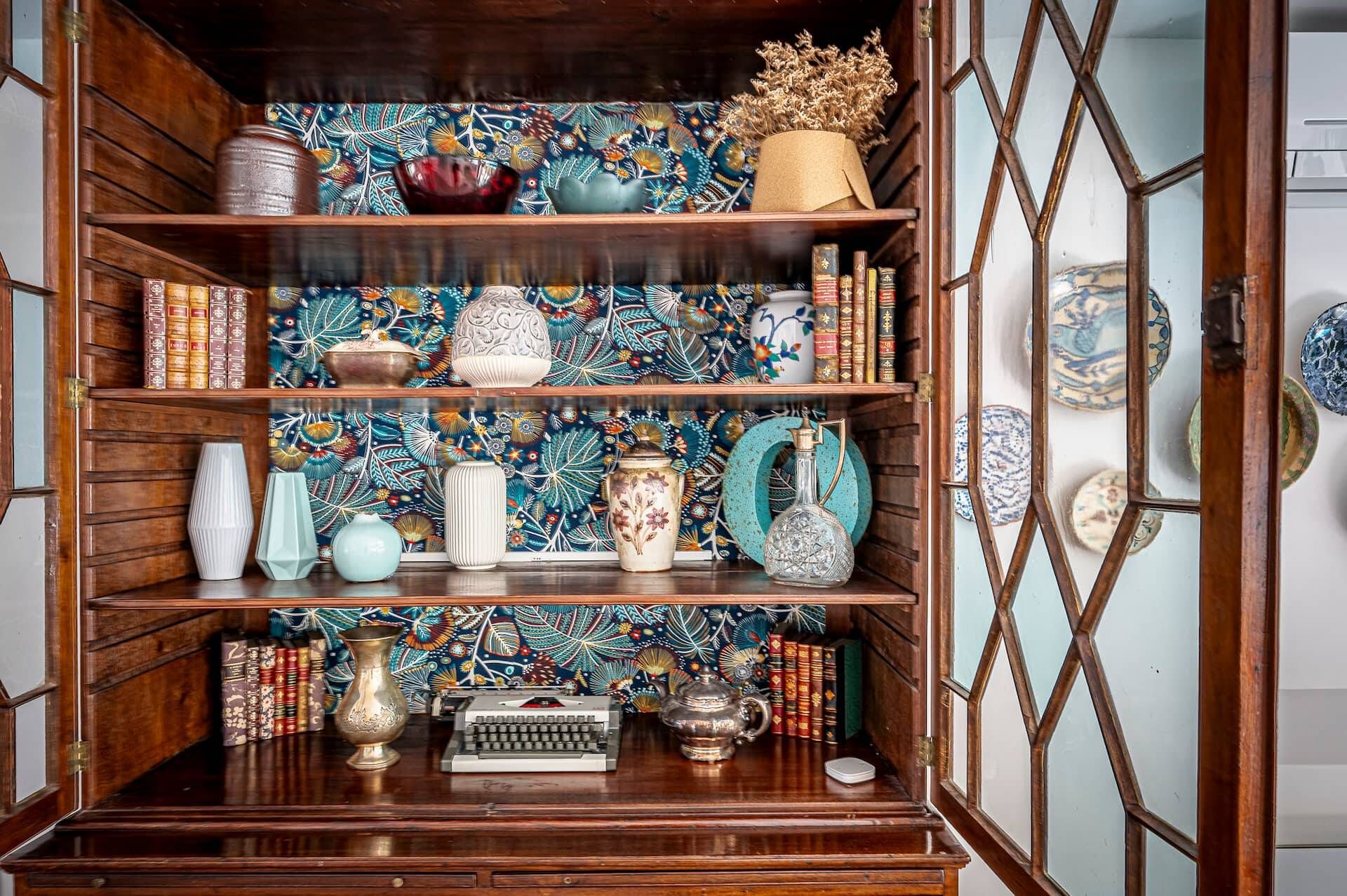 Un meuble en bois doté d’étagères où sont rangés des livres, des vases décoratifs et une machine à écrire.
