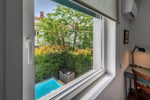 Une chambre avec une fenêtre donnant sur une piscine et un jardin agrémenté d’arbres et d’arbustes.