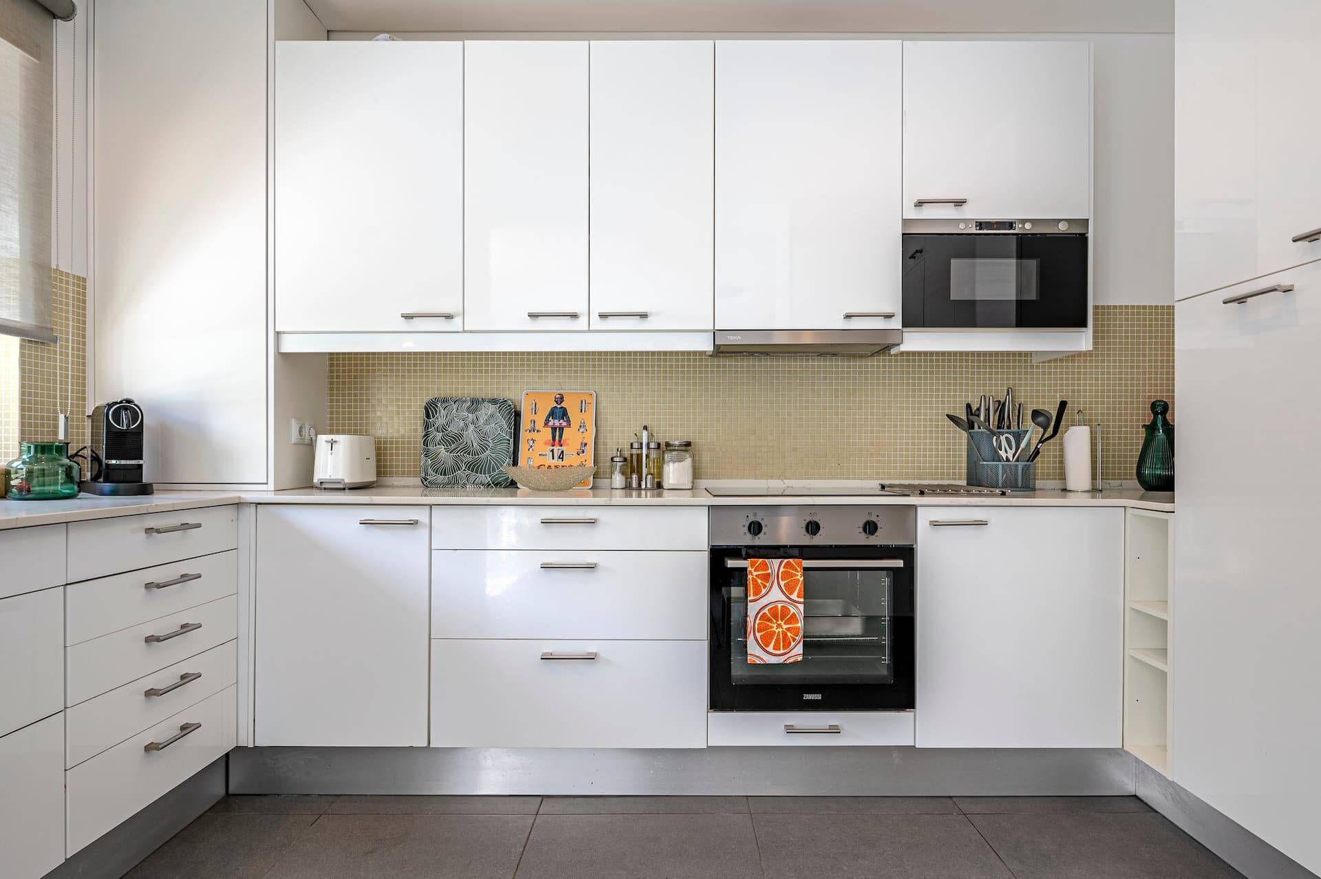 A modern kitchen with white cabinets, a stove, an oven, and a microwave.