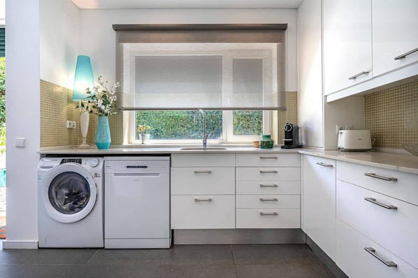 Una cocina moderna con lavadora integrada, ventana con vistas y encimera con cafetera.
