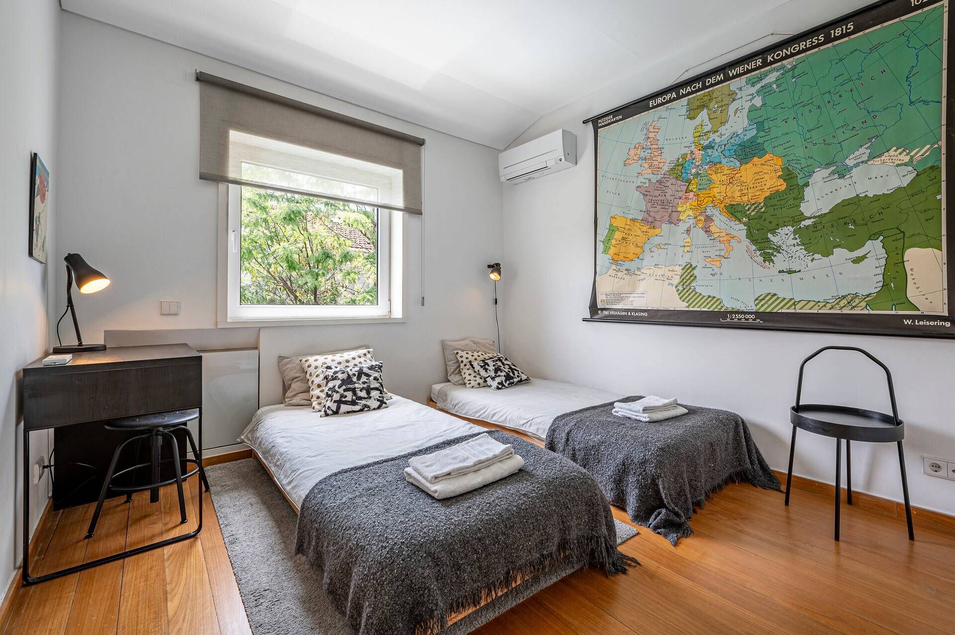 Ein Zimmer mit zwei Betten, einem Schreibtisch, einer Karte an der Wand und einem Fenster.