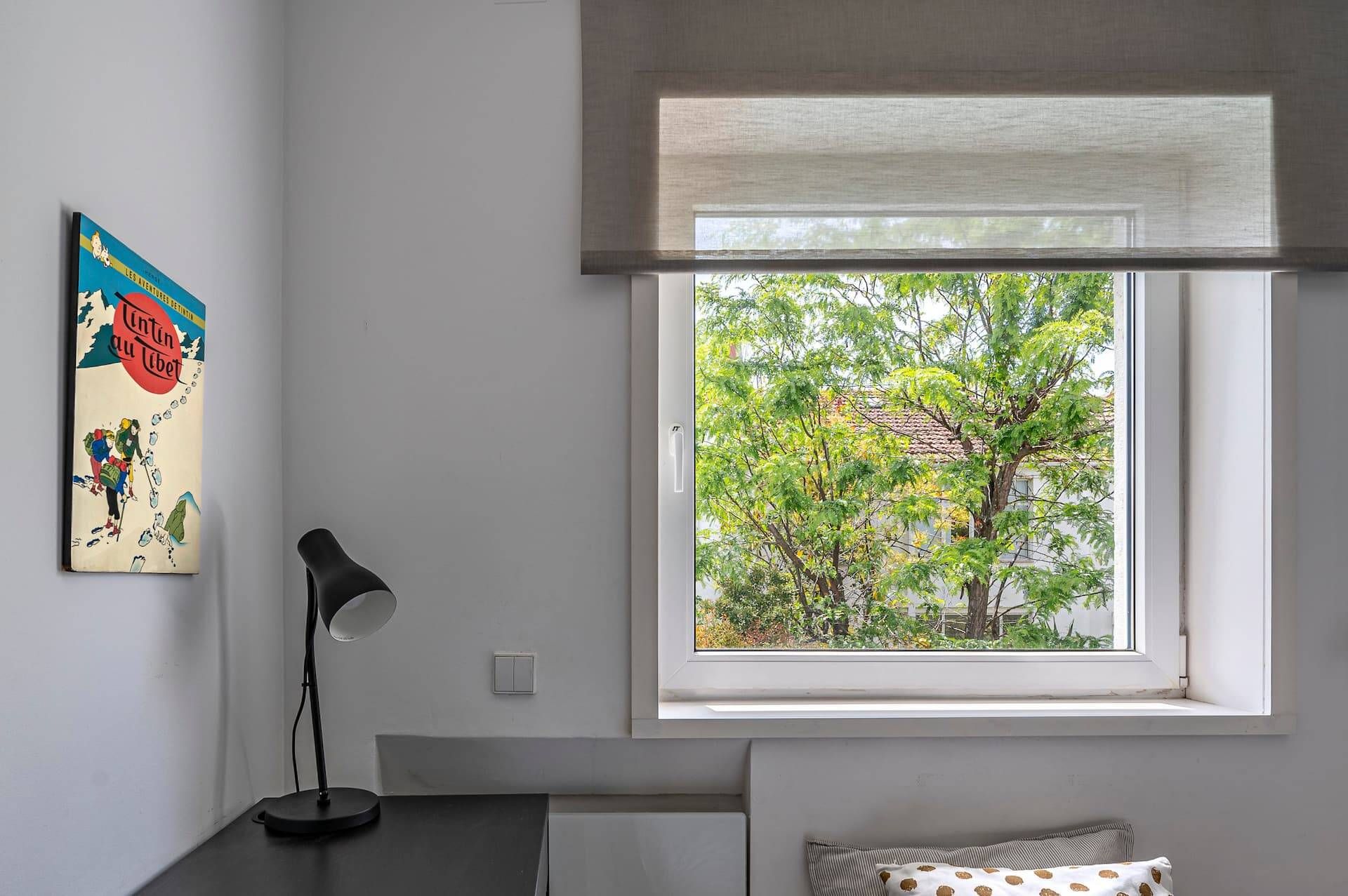 A room with a window, a desk, a lamp, and a wall-mounted picture.