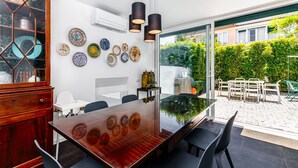 A dining area with a glass-top table, black chairs, and a wooden cabinet. - Clementina: Serene Garden and Pool Stay w/Parking (Lisboa)