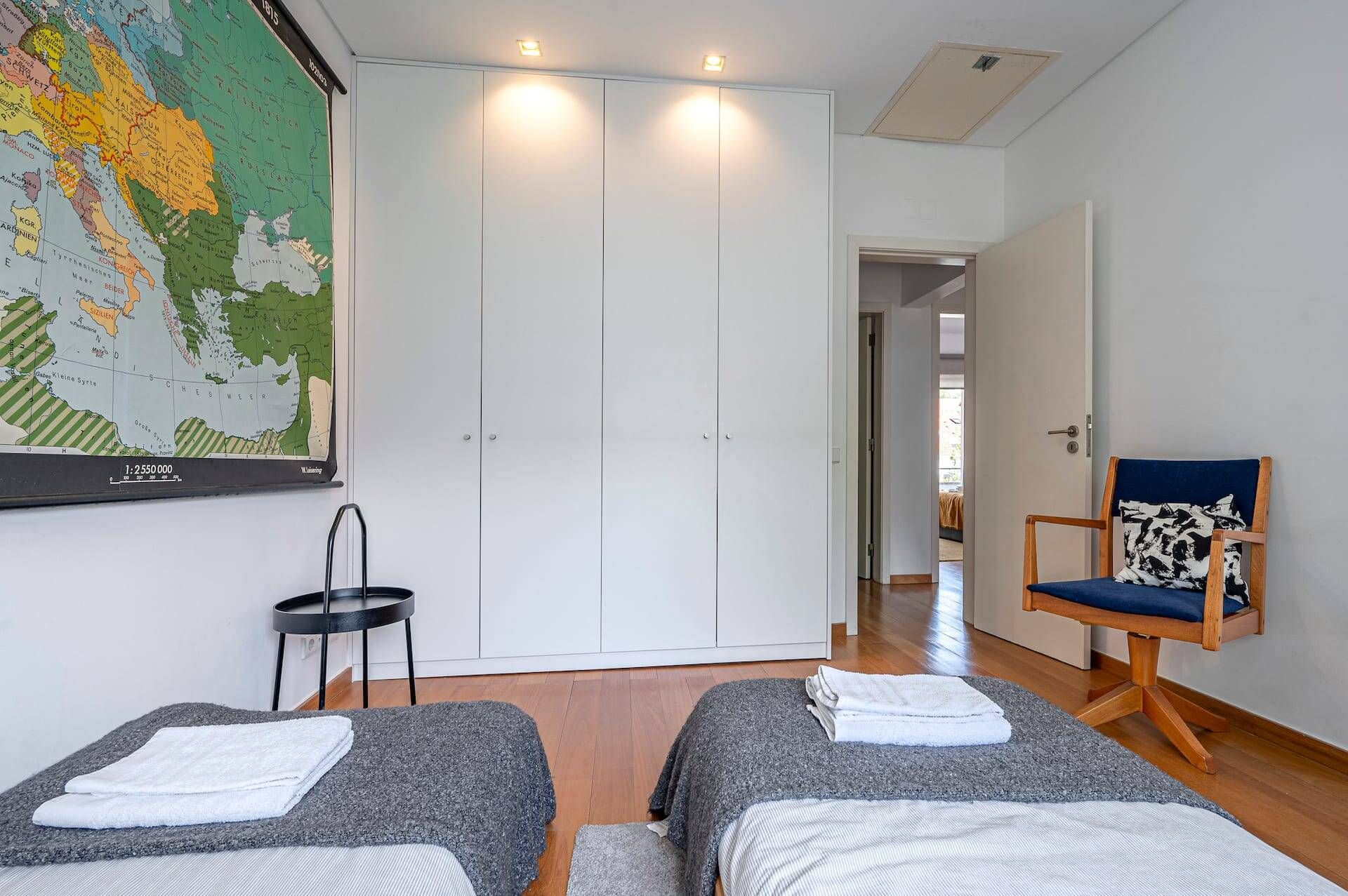 A hotel room with two beds, a map on the wall, a chair, and a wardrobe.