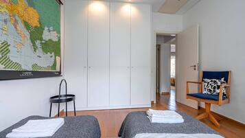 A hotel room with two beds, a map on the wall, a chair, and a wardrobe.
