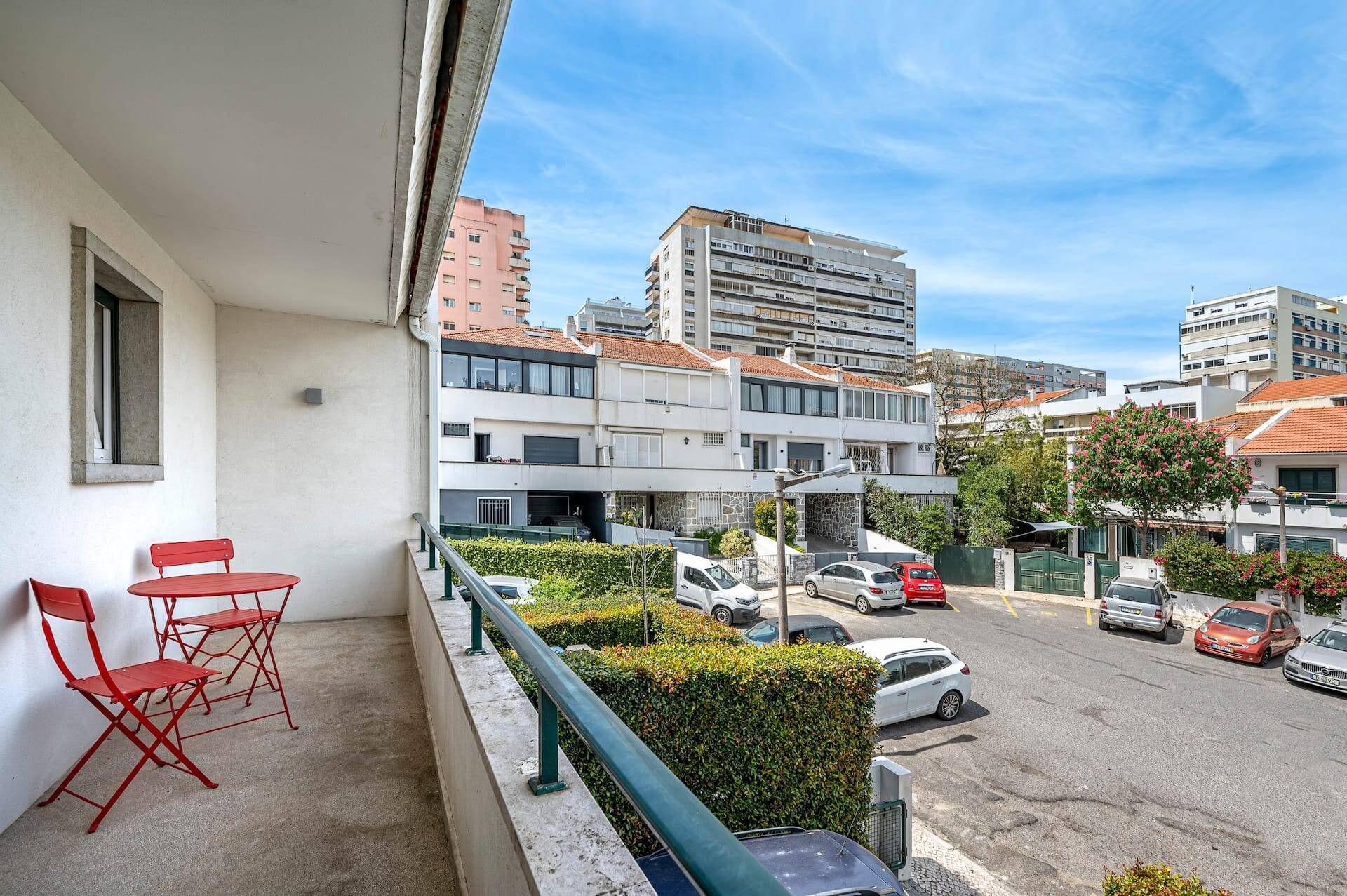 Ein Balkon mit roten Stühlen, Blick auf einen Parkplatz und Gebäude im Hintergrund.