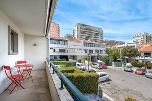 A balcony with red chairs, a view of a parking area, and buildings in the background.