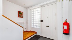 A staircase with wooden steps leading to a landing, a white door with a window, and a red fire extinguisher mounted on the wall. - Clementina: Serene Garden and Pool Stay w/Parking (Lisboa)