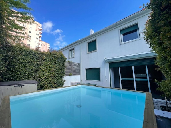 A modern building with a swimming pool, a covered patio, and a view of a cityscape.