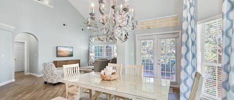 A spacious dining area with a large glass table, white chairs, and a decorative chandelier.