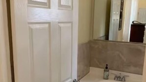 Ein Badezimmer mit einer weißen Tür, einem Waschbecken mit Spiegel darüber und einem Schrank darunter.