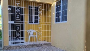 Ein überdachter Patio-Bereich mit Fliesenboden, einem weißen Stuhl und einem Gittertor.