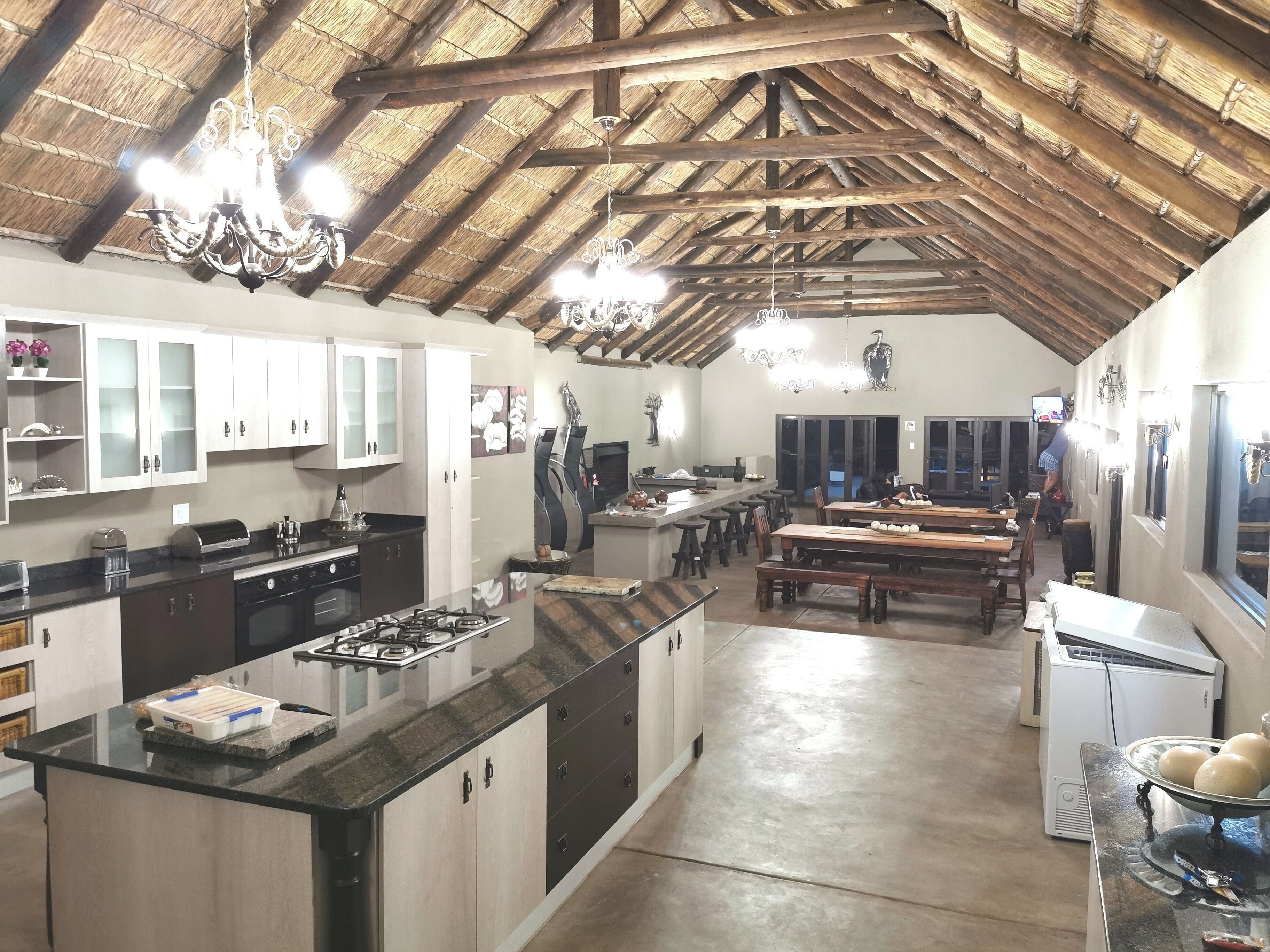 A spacious kitchen with a large island, wooden cabinets, and a thatched ceiling.