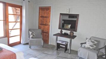 Une pièce comprenant un lit, deux fauteuils, une petite table avec un miroir et une porte.
