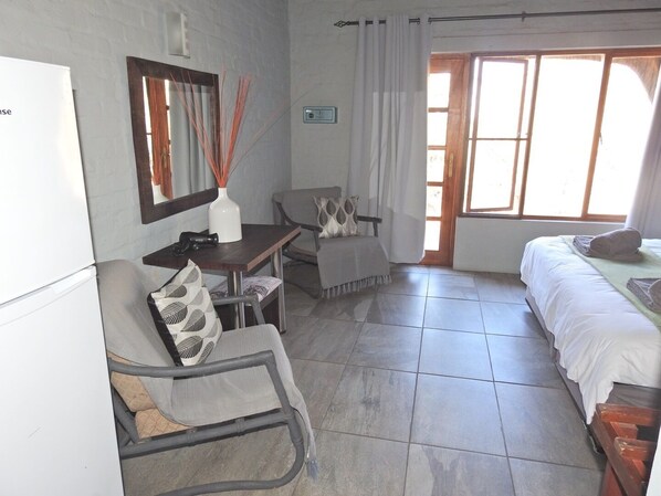 Una habitación de hotel compacta con cama, escritorio, silla y una mesita.