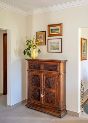 Een houten kast met meerdere lades, een vaas met gele bloemen, en drie kunstwerken in lijsten aan de muur.