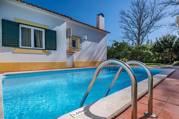 Una piscina con una escalera de metal, cielo despejado y un edificio con tejado de azulejos.