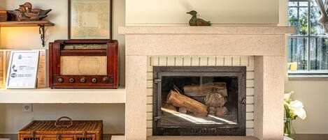 Una chimenea con leña, un radio y objetos decorativos en estantes.