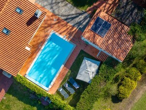 An aerial view of a residential property with a swimming pool, a covered patio, and a solar panel.
