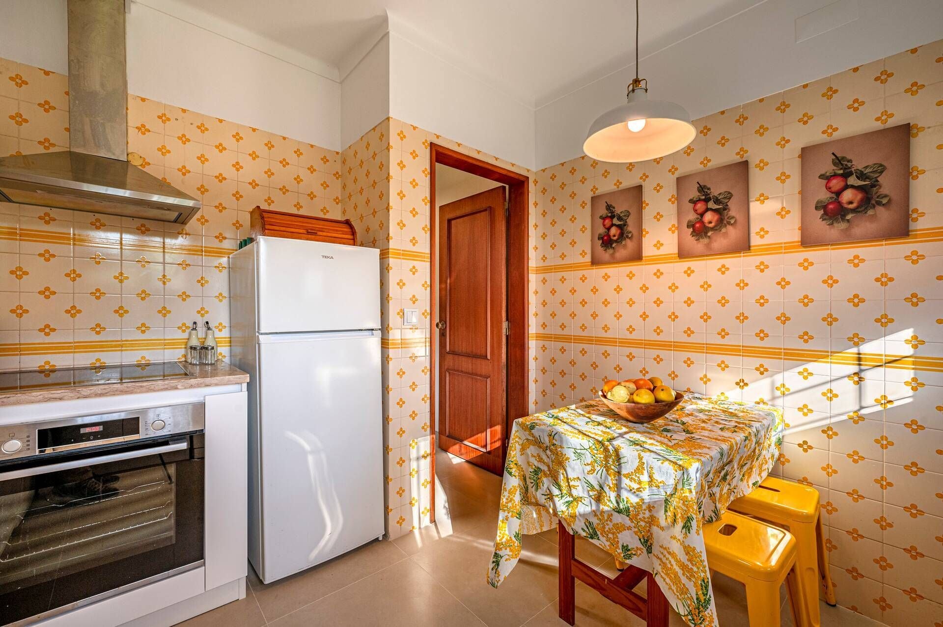 Una cocina con refrigerador, horno y una mesa con mantel estampado.