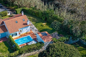 A house with a swimming pool, a garden, and a view of the surrounding area.