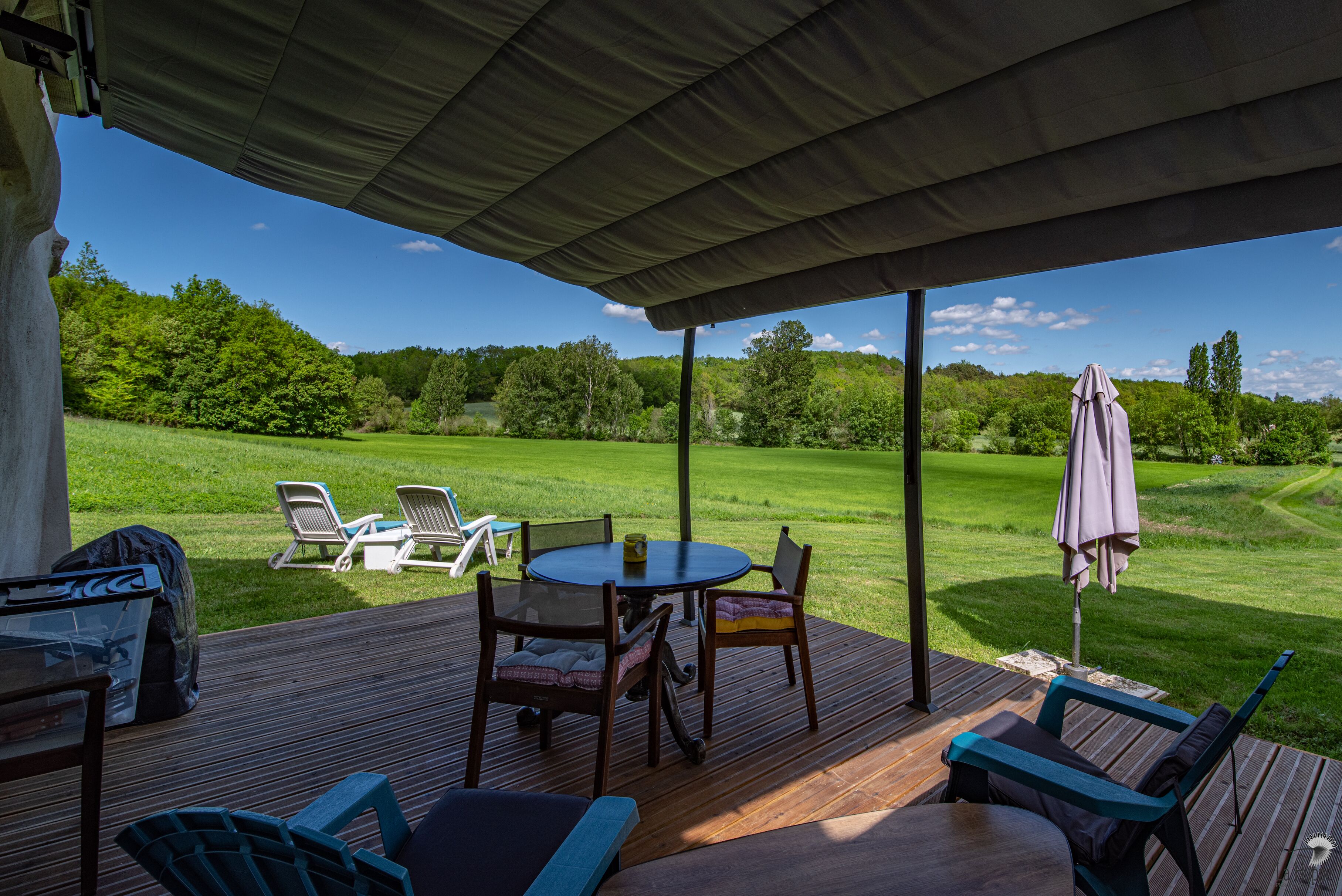 An outdoor patio with a table and chairs, a covered area, and a view of a green landscape.