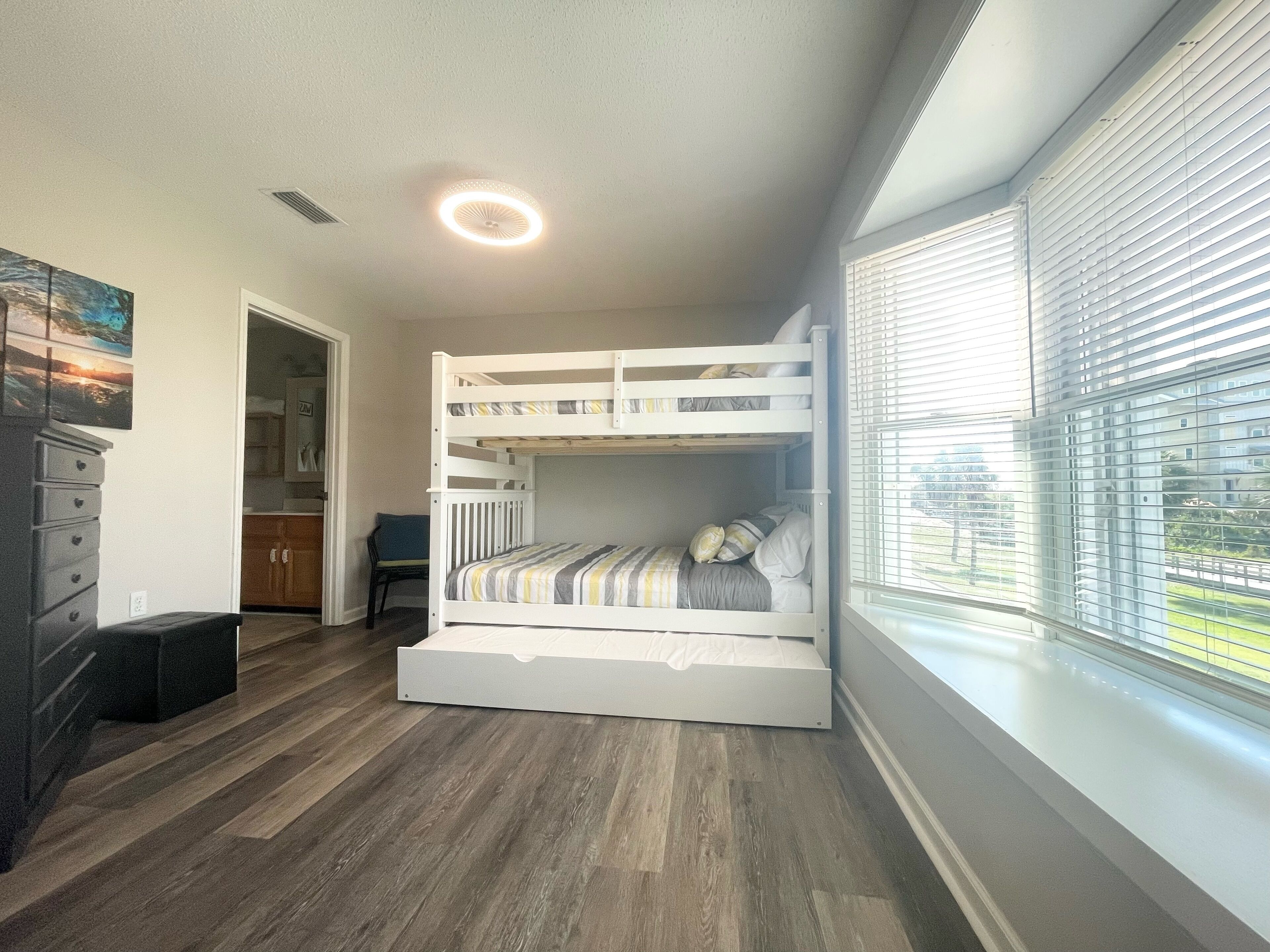 A bunk bed with a view of the outdoors through large windows, a wooden floor, and a ceiling light.