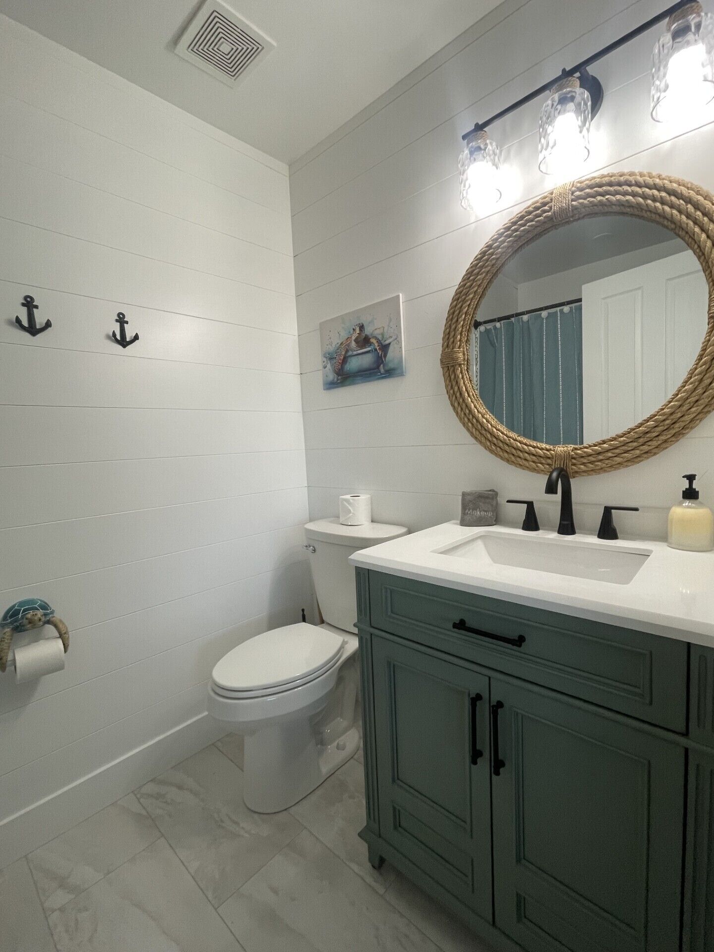 A bathroom with white tiled walls, a white toilet, a green vanity with a round mirror, and two wall-mounted lights.