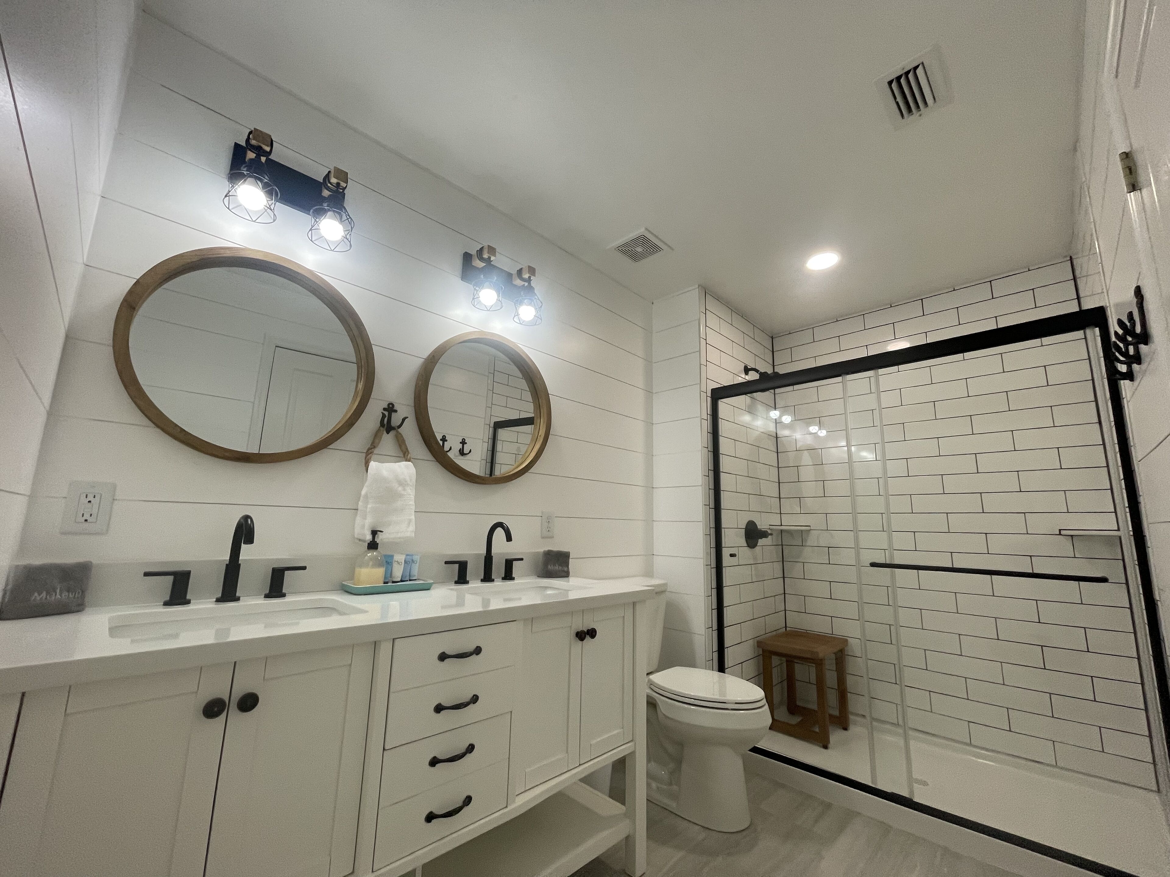 Een moderne badkamer met een wit wastafelmeubel, twee ronde spiegels, een toilet en een douche met glazen wanden.