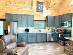 A modern kitchen with grey cabinets, stainless steel appliances, and a leather chair. - Cabin w/Breathtaking Views, Hot Tub & Game Room (Sevierville)