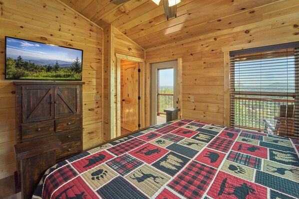A wooden cabin room with a large bed, a television, and a door leading to a balcony.