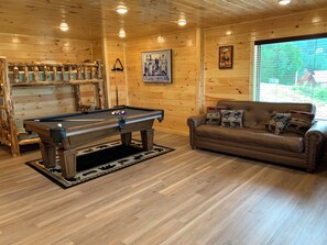 A wooden interior with a pool table, a leather sofa with patterned cushions, and a poster on the wall. - Cabin w/Breathtaking Views, Hot Tub & Game Room (Sevierville)