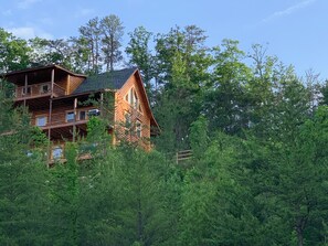 A multi-story log cabin with balconies, surrounded by dense forest.