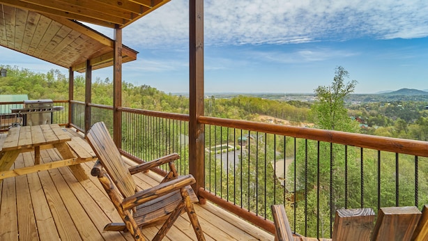 A wooden deck with rocking chairs and a grill, overlooking a scenic landscape with trees and hills. - Cabin w/Breathtaking Views, Hot Tub & Game Room (Sevierville)