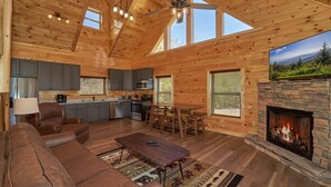 A spacious living room with a fireplace, a kitchen area, and a dining space. - Cabin w/Breathtaking Views, Hot Tub & Game Room (Sevierville)