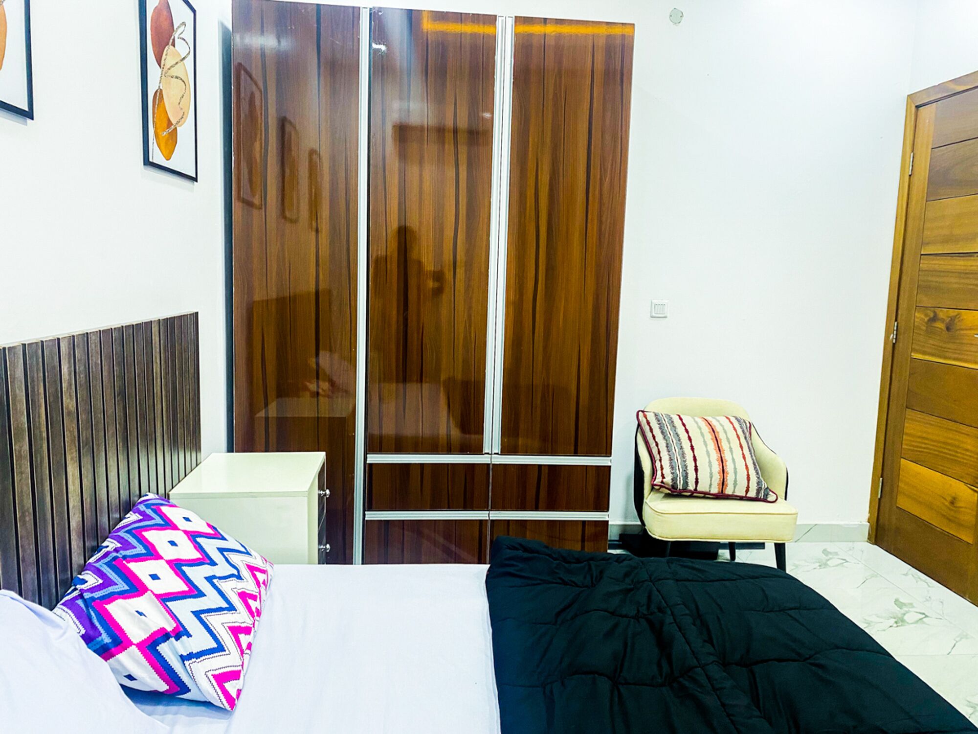 A bedroom with a bed, a chair, a wardrobe, and a bedside table.