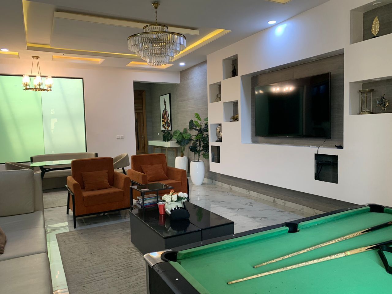 A modern living room with a pool table, comfortable seating, a large TV, and decorative shelves.