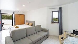 A modern hotel room with a bed, grey sofa, and a small desk with a TV. - Apartamentos Vale de Carros by Umbral (Albufeira)