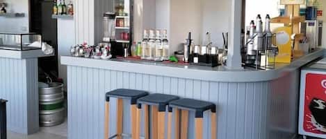 Una zona de bar con taburetes, un refrigerador y estantes con botellas.