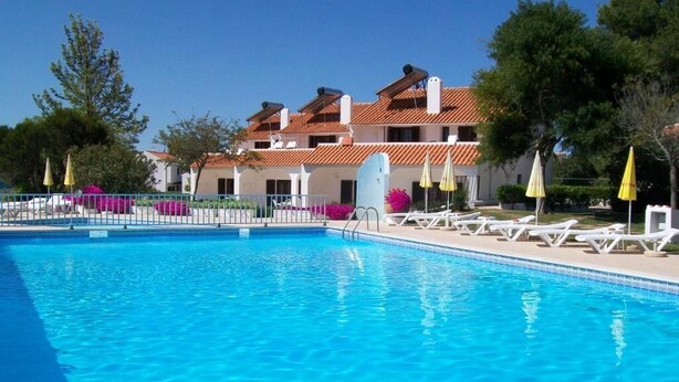A swimming pool with clear blue water, surrounded by white lounge chairs and yellow umbrellas. - Apartamentos Vale de Carros by Umbral (Albufeira)