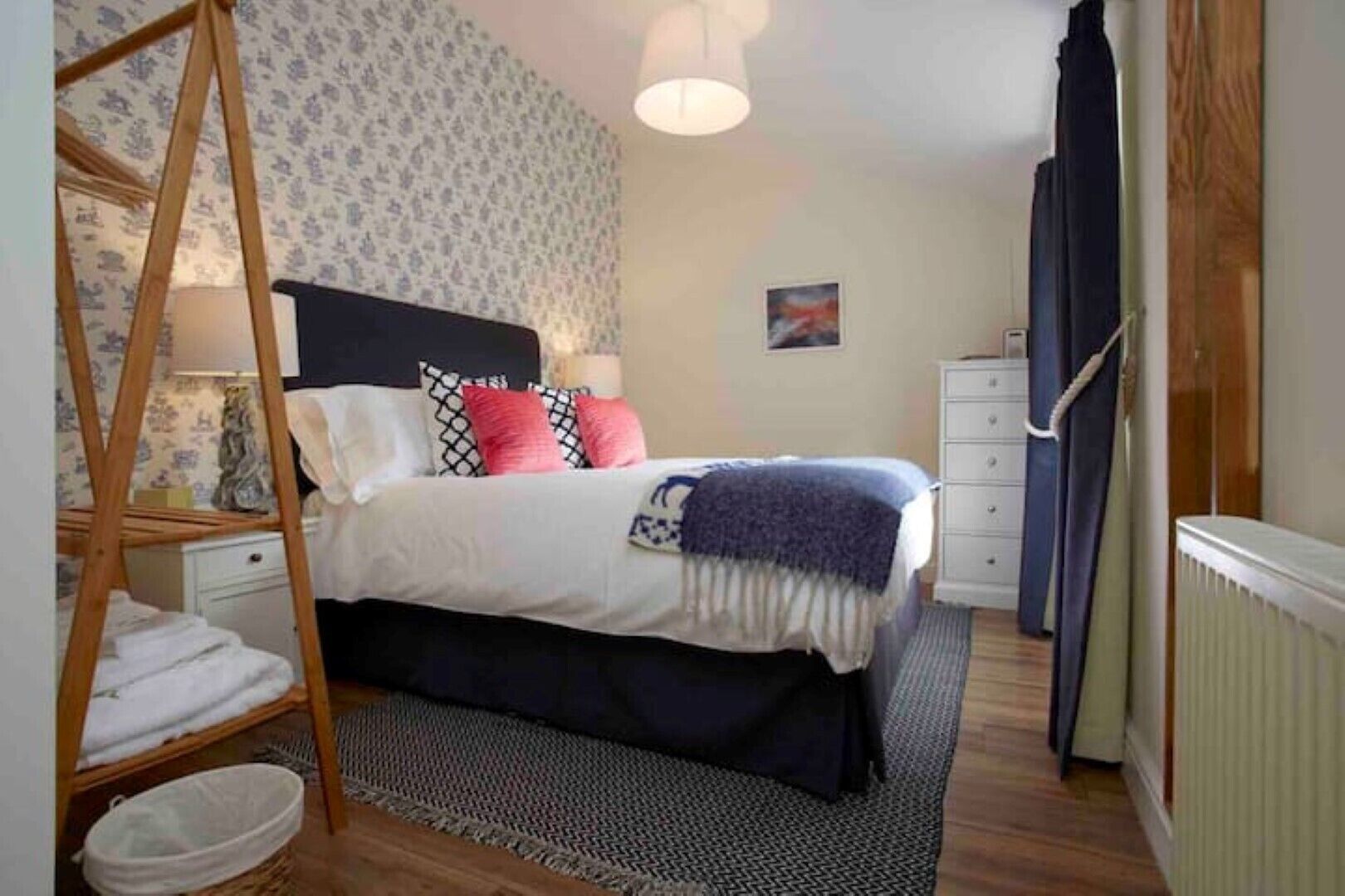 A bedroom with a bed, bedside tables, a hanging chair, a radiator, and a dresser.