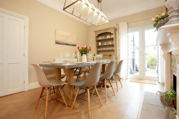 Un coin repas avec une table et des chaises en bois, un lustre et une vue sur l’extérieur grâce à une porte vitrée.