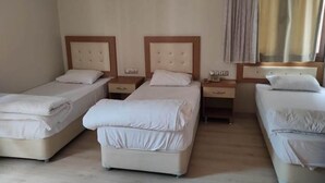 A hotel room with two single beds, a bedside table with a lamp, an air conditioner, and a window with curtains. - Şato Otel (Adana)