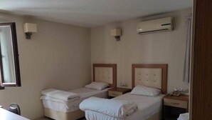 A hotel room with two single beds, a desk, a chair, and an air conditioning unit. - Şato Otel (Adana)