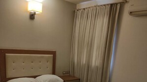 A hotel room with a bed, a nightstand, a lamp, a chair, and a window with curtains. - Şato Otel (Adana)