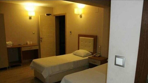 A hotel room with two single beds, a bedside table with a lamp, a desk with a chair, and a wardrobe. - Şato Otel (Adana)