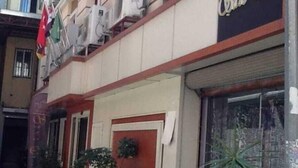 A hotel facade with air conditioning units, a red door, and potted plants. - Şato Otel (Adana)